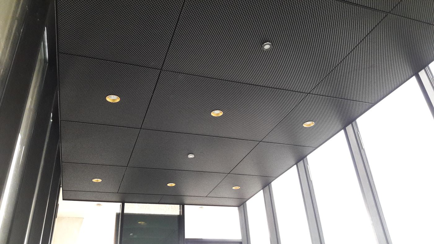 Dunkle gelochte Metalldecke im Eingangsbereich mit eingebauten Downlights